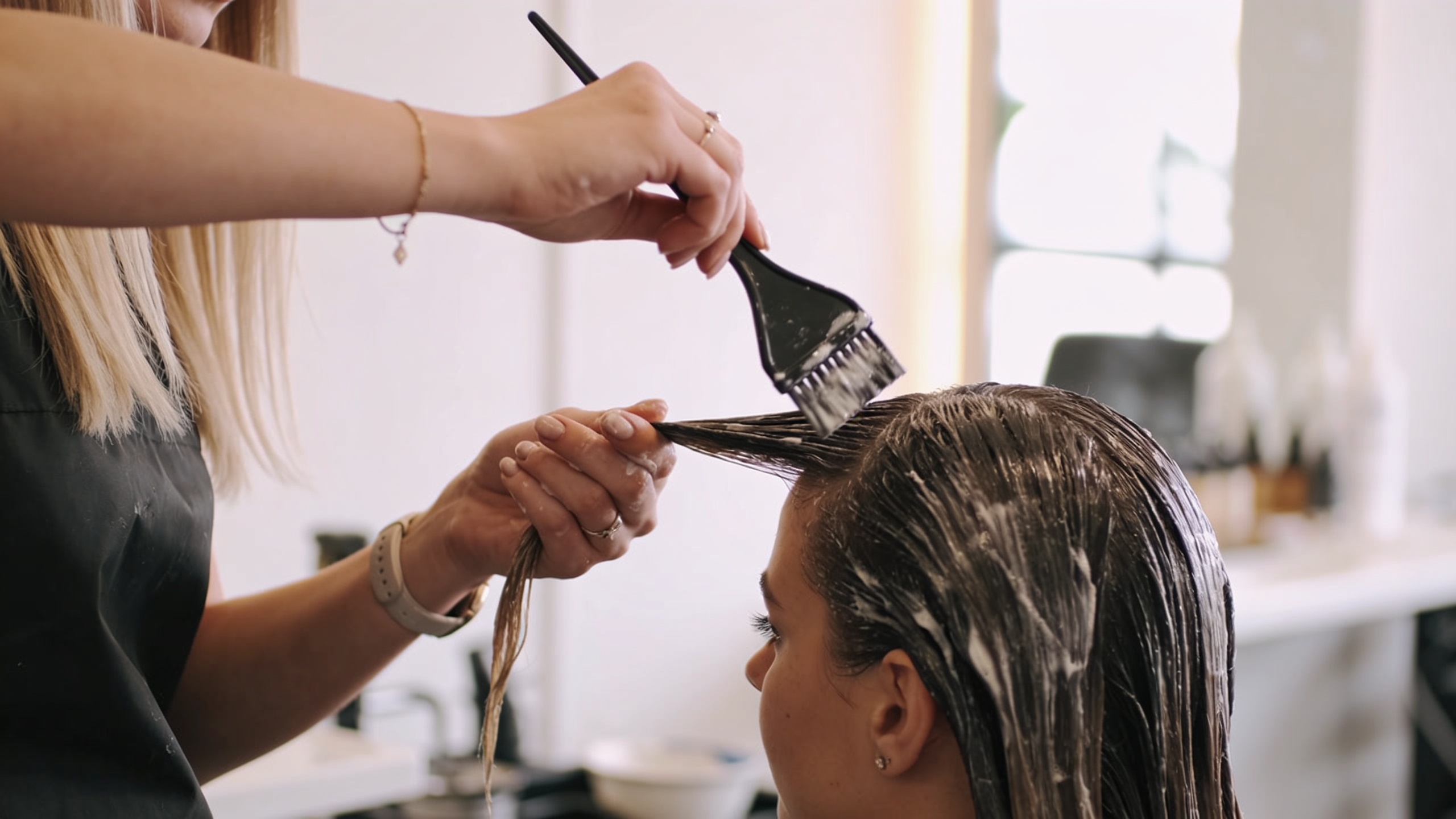 Cosmetologist applying hair color to a client in a modern salon